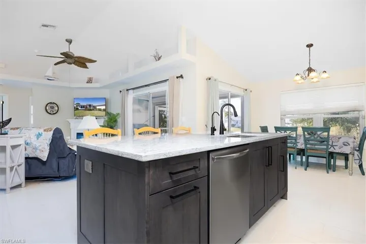 Kitchen featuring dishwasher, a center island with sink, open floor plan, light stone counters, and a ceiling fan