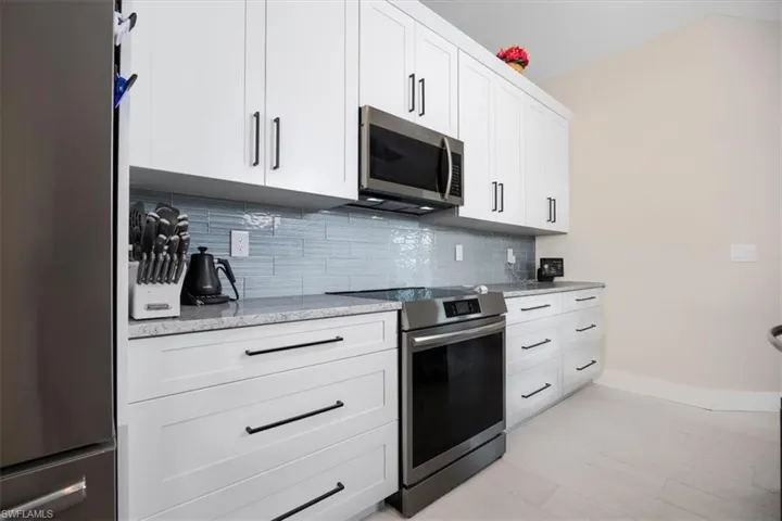 Kitchen featuring stainless steel appliances, white cabinetry, light stone counters, and tasteful backsplash