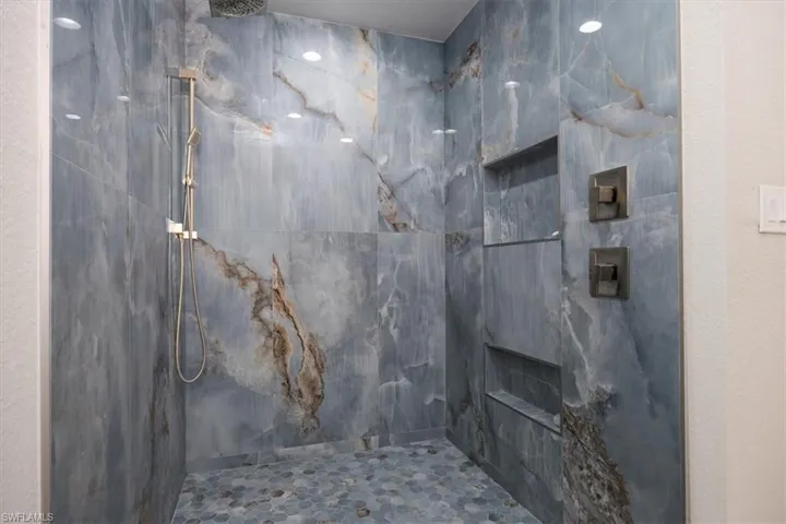 Bathroom with a marble finish shower and a textured wall