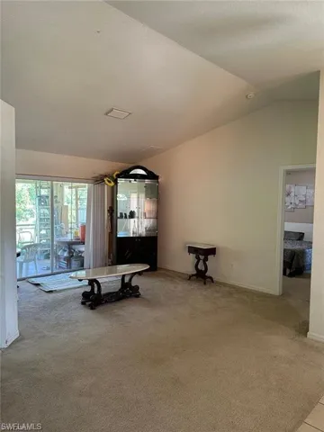 Unfurnished living room with light colored carpet and vaulted ceiling
