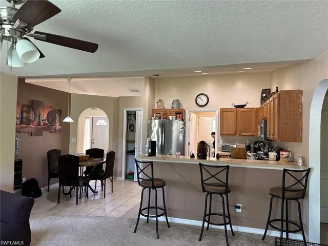 Kitchen featuring ceiling fan, light tile patterned floors, appliances with stainless steel finishes, kitchen peninsula, and a breakfast bar area