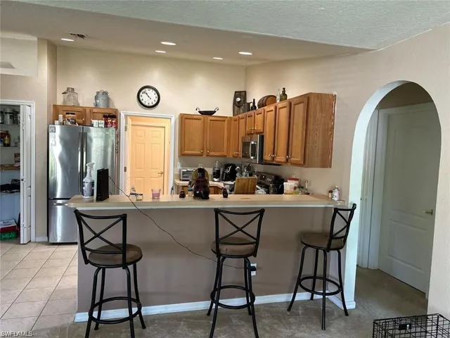 Kitchen with stainless steel appliances, a kitchen breakfast bar, kitchen peninsula, a textured ceiling, and light tile patterned flooring