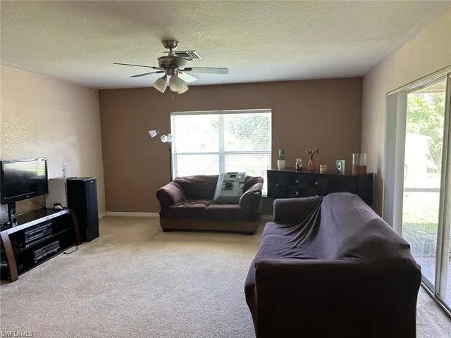 Carpeted living room featuring a wealth of natural light, ceiling fan, and a textured ceiling