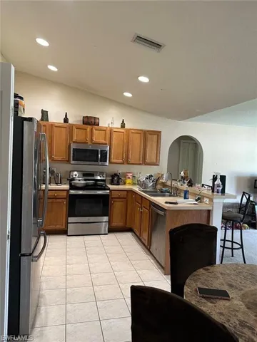 Kitchen featuring kitchen peninsula, appliances with stainless steel finishes, vaulted ceiling, sink, and light tile patterned flooring