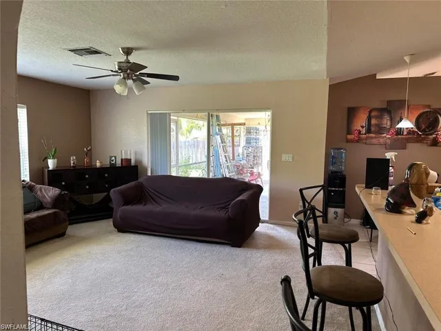 Carpeted living room featuring a textured ceiling, ceiling fan, and lofted ceiling