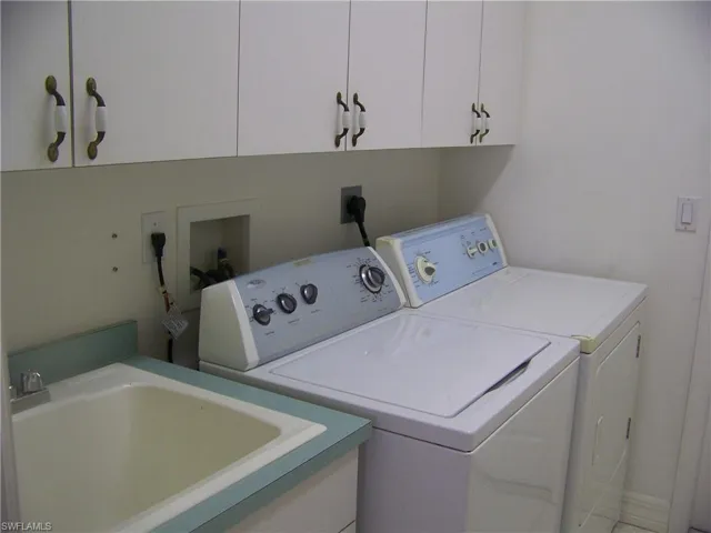 Laundry area featuring washing machine and clothes dryer, utility sink, and cabinets located off kitchen.