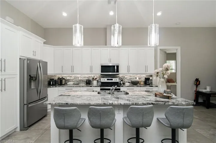 Kitchen featuring white cabinetry, stainless steel appliances, a large island with a stone countertop, and pendant lighting