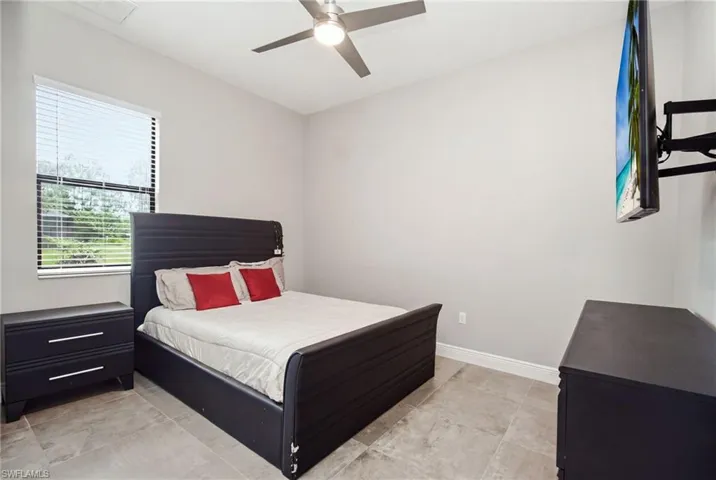 Tile flooring, window with horizontal blinds, overhead ceiling fan, neutral wall tones, and a wall-mounted television bracket