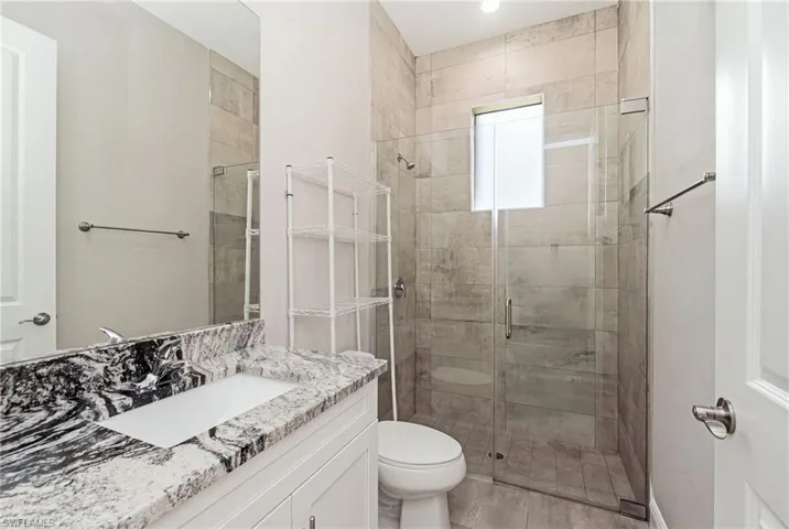 Spacious bathroom featuring a single vanity with stone countertop, large wall mirror, and an enclosed walk-in shower with tile surround and a transom window