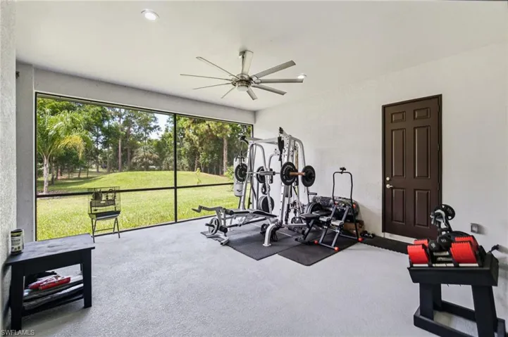 Screened enclosure with expansive backyard views, featuring a ceiling fan, recessed lighting, and a paneled exterior door