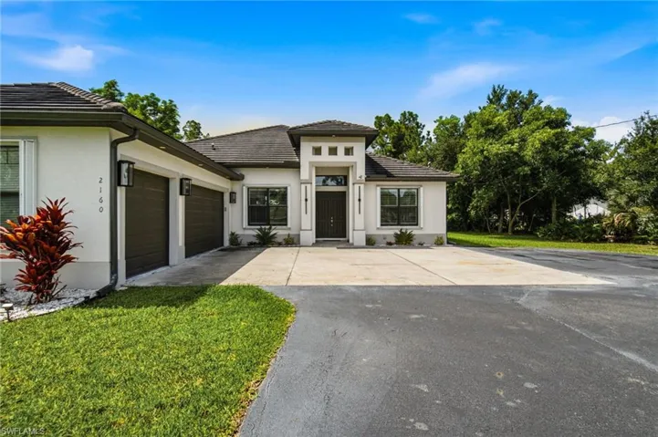 Contemporary stucco exterior, two-car garage, concrete driveway, tiled roof, and established landscaping