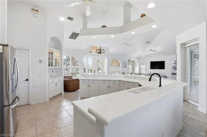 Kitchen featuring open floor plan, glass insert cabinets, stainless steel refrigerator with ice dispenser, recessed lighting, and high vaulted ceiling