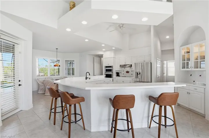 Kitchen with white cabinetry, decorative backsplash, a kitchen bar, glass insert cabinets, and stainless steel appliances