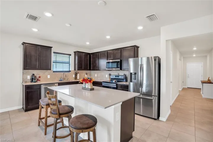 Kitchen with stainless steel appliances, dark brown cabinetry, backsplash, a kitchen island, and a breakfast bar