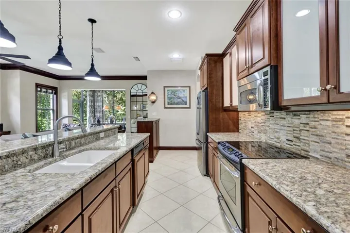 Kitchen featuring light tile patterned flooring, stainless steel appliances, tasteful backsplash, a sink, and hanging light fixtures