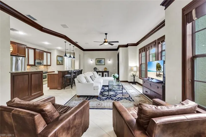 Living area featuring light tile patterned flooring, visible vents, baseboards, ornamental molding, and a ceiling fan