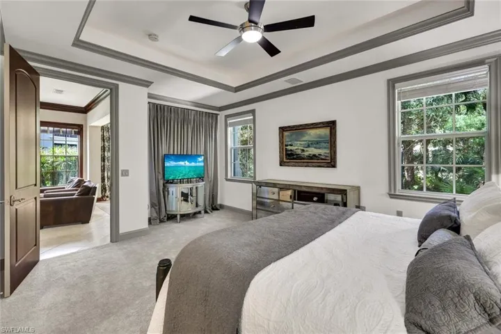 Carpeted bedroom with crown molding, baseboards, a raised ceiling, ceiling fan, and visible vents