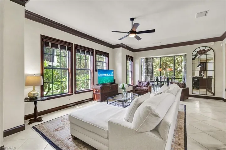 Living room featuring crown molding, light tile patterned floors, baseboards, visible vents, and ceiling fan