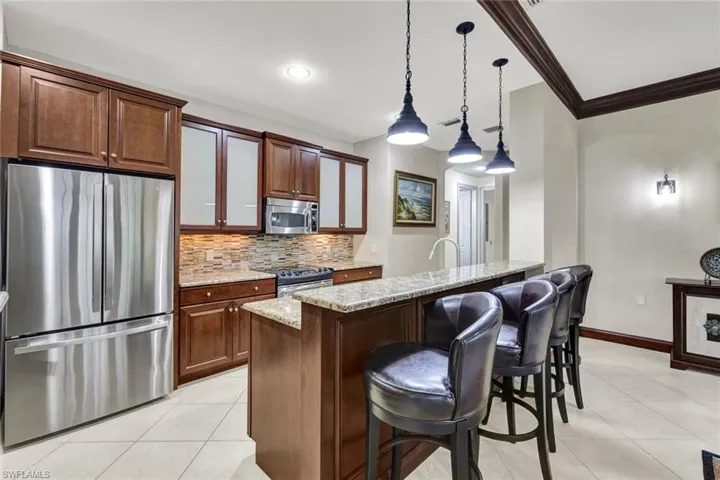 Kitchen with a kitchen breakfast bar, tasteful backsplash, ornamental molding, light stone counters, and appliances with stainless steel finishes