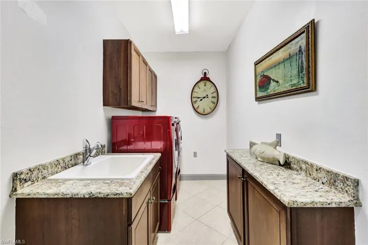Laundry area with a sink, washing machine and clothes dryer, light tile patterned floors, baseboards, and cabinet space