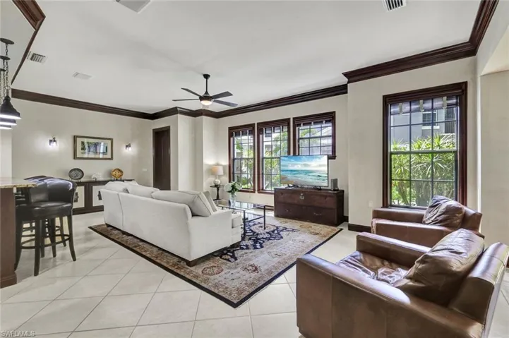 Living area with light tile patterned flooring, visible vents, crown molding, baseboards, and a ceiling fan