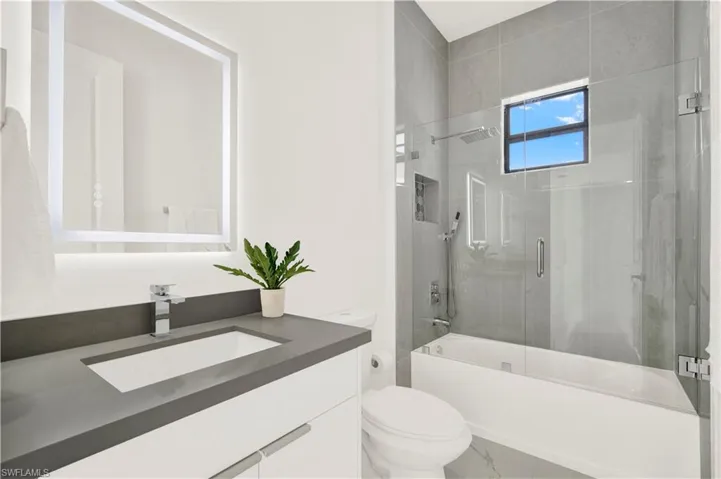 Full bathroom with vanity, bath / shower combo with glass door, and marble look tiles