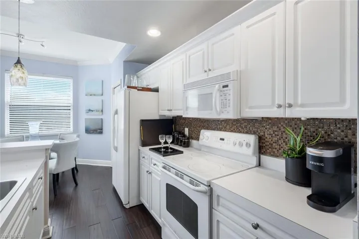 Kitchen featuring white appliances, white cabinets, tasteful backsplash, pendant lighting, and crown molding