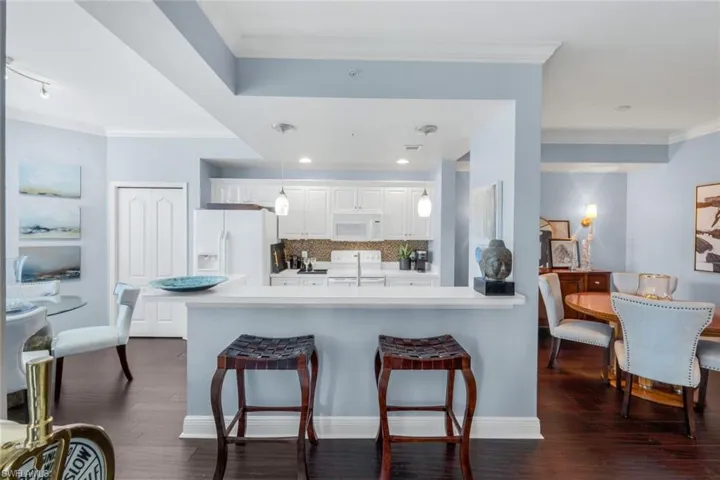 Kitchen with ornamental molding, light countertops, white cabinets, a kitchen bar, and white appliances
