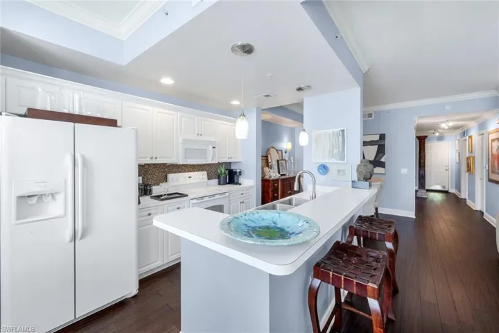 Kitchen with ornamental molding, white appliances, light countertops, white cabinets, and tasteful backsplash