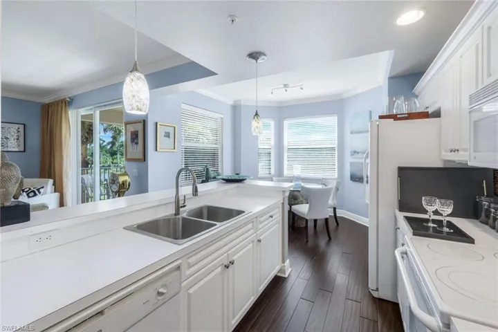 Kitchen featuring white cabinetry, light countertops, white appliances, hanging light fixtures, and ornamental molding