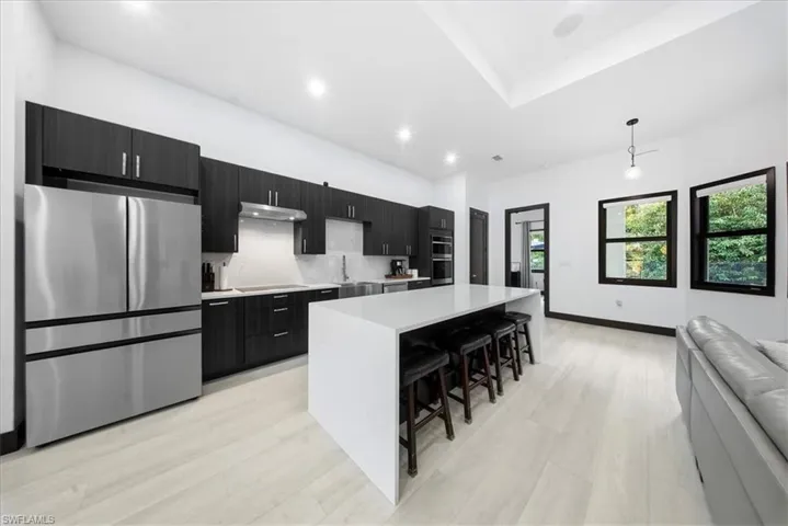 Kitchen featuring dark cabinetry, stainless steel appliances, a kitchen island, pendant lighting, and a kitchen bar
