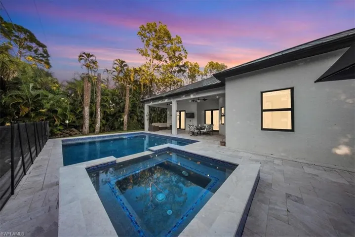 Pool at dusk with a patio area, a pool with connected hot tub, and outdoor dining space
