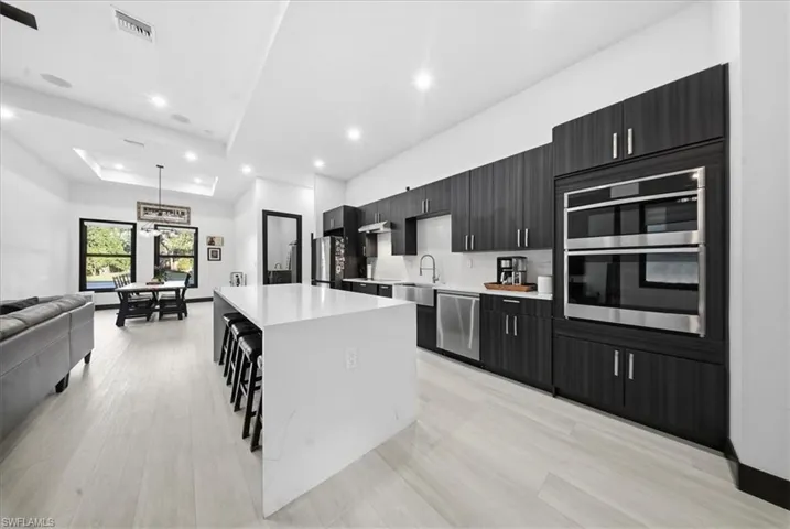 Kitchen featuring dark cabinetry, open floor plan, a large island, a raised ceiling, and a kitchen bar