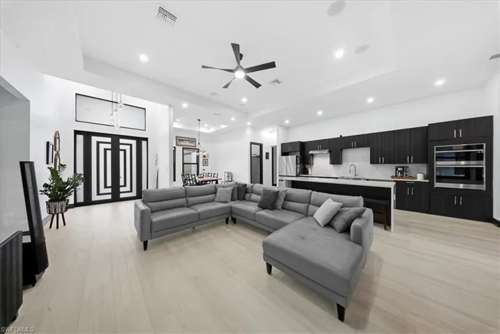Living area with ceiling fan, a raised ceiling, light wood-style flooring, recessed lighting, and a high ceiling