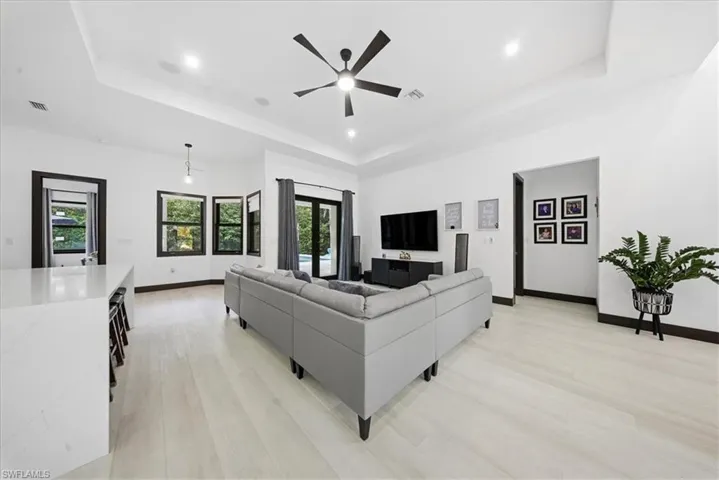 Living room with light wood-type flooring, a raised ceiling, a ceiling fan, and recessed lighting