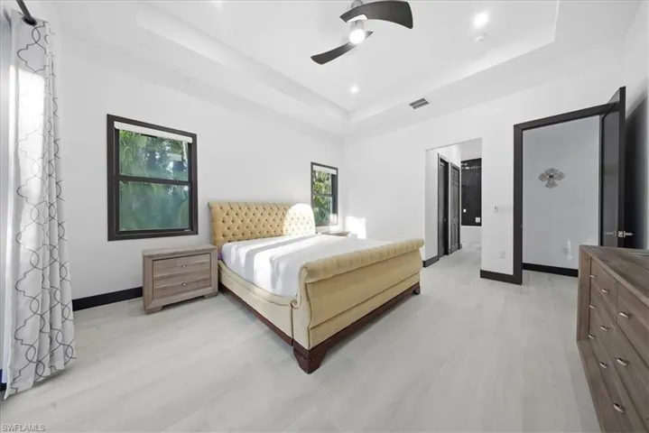 Bedroom featuring ceiling fan, light wood finished floors, and a tray ceiling