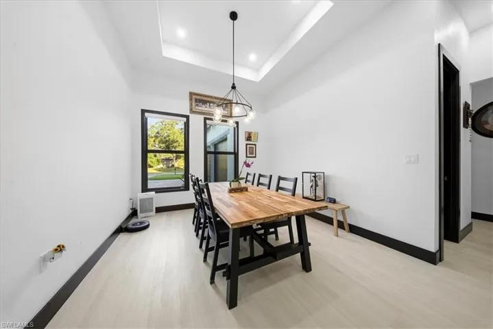 Dining area featuring a raised ceiling, light wood-type flooring, a chandelier, and a high ceiling