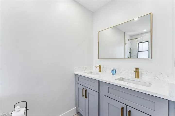 Full bathroom with walk in shower, double vanity, and baseboards