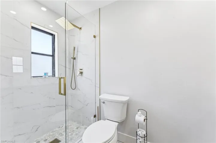 Bathroom with toilet, a marble finish shower, and baseboards