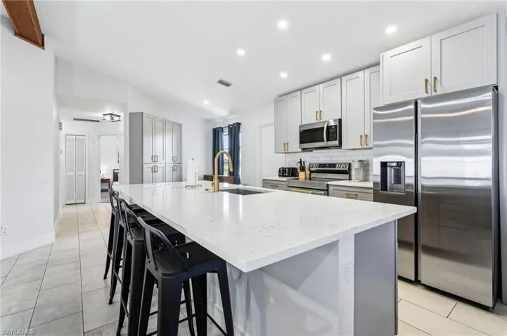Kitchen featuring appliances with stainless steel finishes, a sink, a large island with sink, light stone countertops, and light tile patterned floors