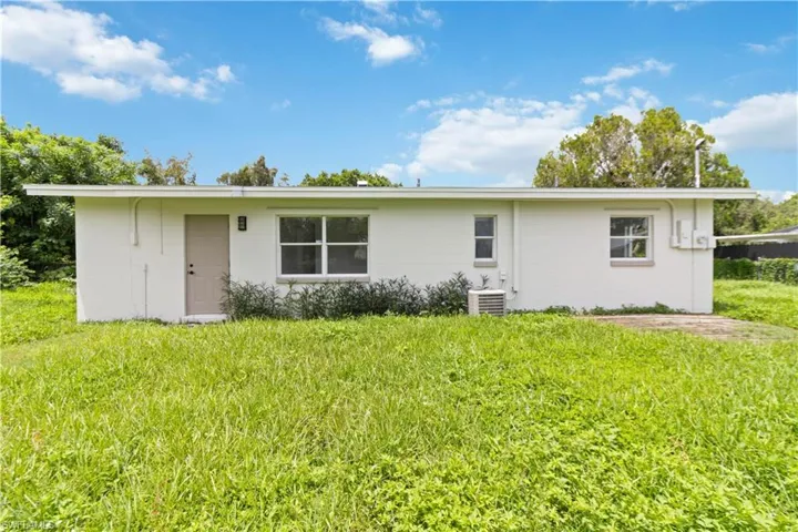 Rear view of house featuring a lawn and central AC