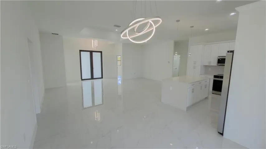 Kitchen featuring white cabinetry, a kitchen island, stainless steel appliances, open floor plan, and suspended lighting