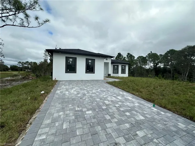 View of front of home featuring decorative driveway, stucco siding, and a front lawn