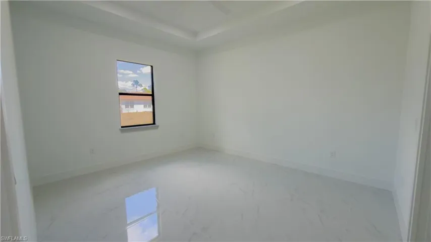 Empty room featuring light marble finish floors, a ceiling fan, and a raised ceiling