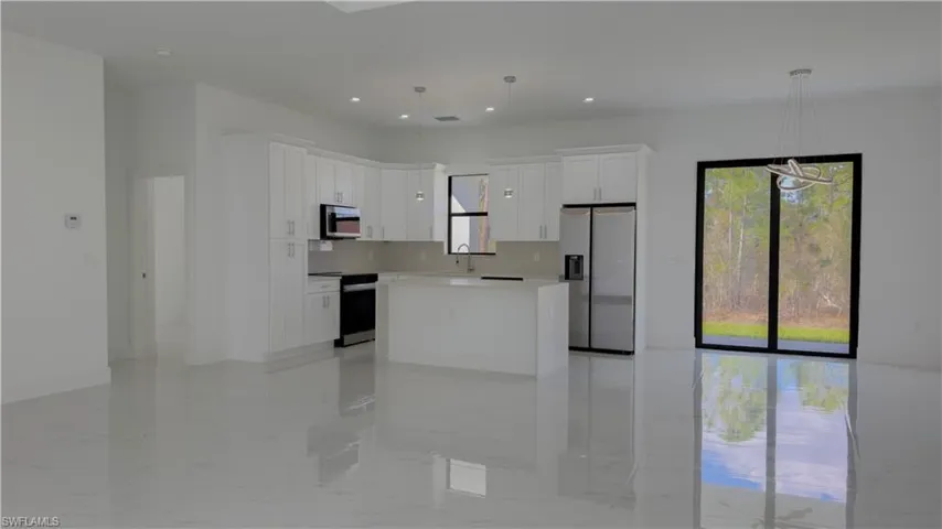 Kitchen with stainless steel appliances, a kitchen island, white cabinetry, and pendant lighting