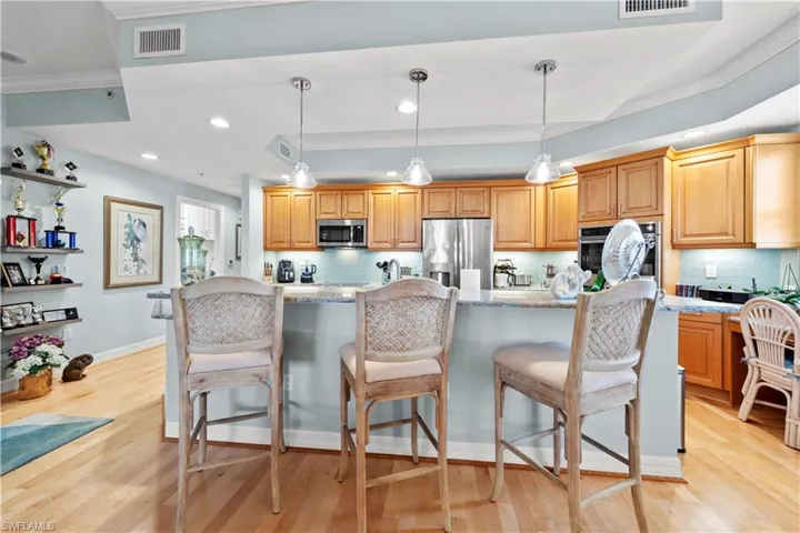 Kitchen with appliances with stainless steel finishes, backsplash, light stone countertops, a center island, and ornamental molding