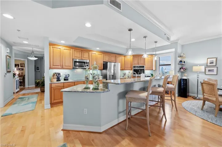 Kitchen with stainless steel appliances, light stone countertops, a large island, light wood-style floors, and tasteful backsplash