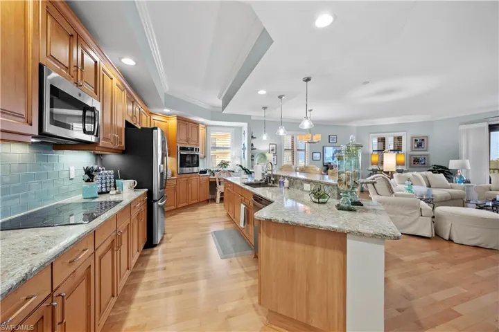 Kitchen with stainless steel appliances, light wood-style flooring, open floor plan, backsplash, and ornamental molding
