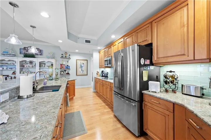 Kitchen featuring stainless steel appliances, crown molding, tasteful backsplash, light wood finished floors, and a tray ceiling