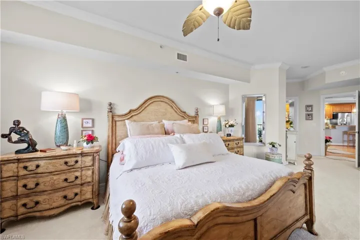 Carpeted bedroom featuring stainless steel refrigerator with ice dispenser, crown molding, and a ceiling fan